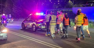 Oznakowany radiowóz oraz motocykle policyjne podczas zabezpieczenia przejazdu osób na łyżworolkach. Za radiowozem uczestnicy rajdu na łyżworolkach.