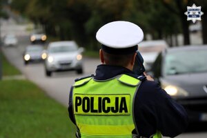 Umundurowany Policjant Wydziału Ruchu Drogowego dokonujący pomiaru prędkości nadjeżdżających pojazdów.